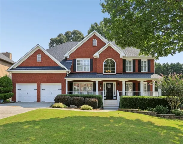 Traditional brick exterior featuring a covered front porch with white railing, a double-door garage, and an arched window accent