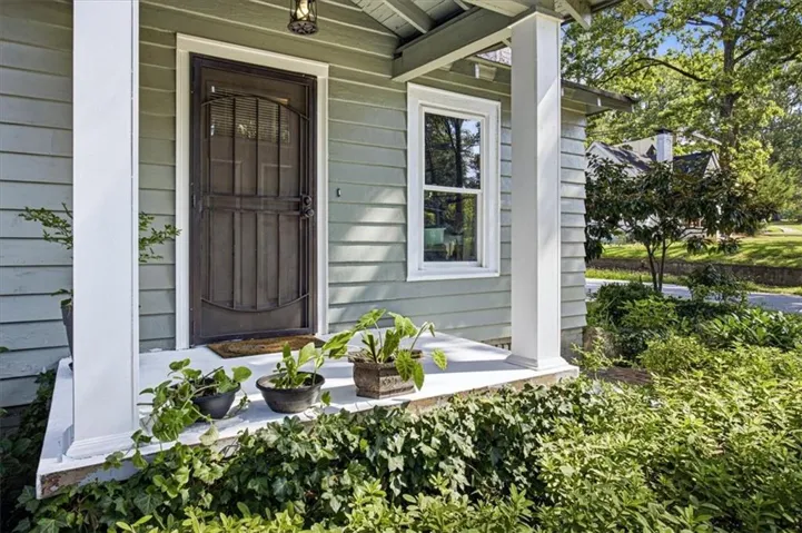 Exterior siding with horizontal panels, prominent front porch, white support columns, dark entry door with decorative security screen, and a visible window with white trim