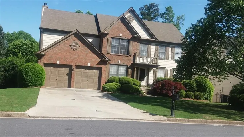 Traditional-style house featuring concrete driveway, a front lawn, brick siding, a garage, and a chimney