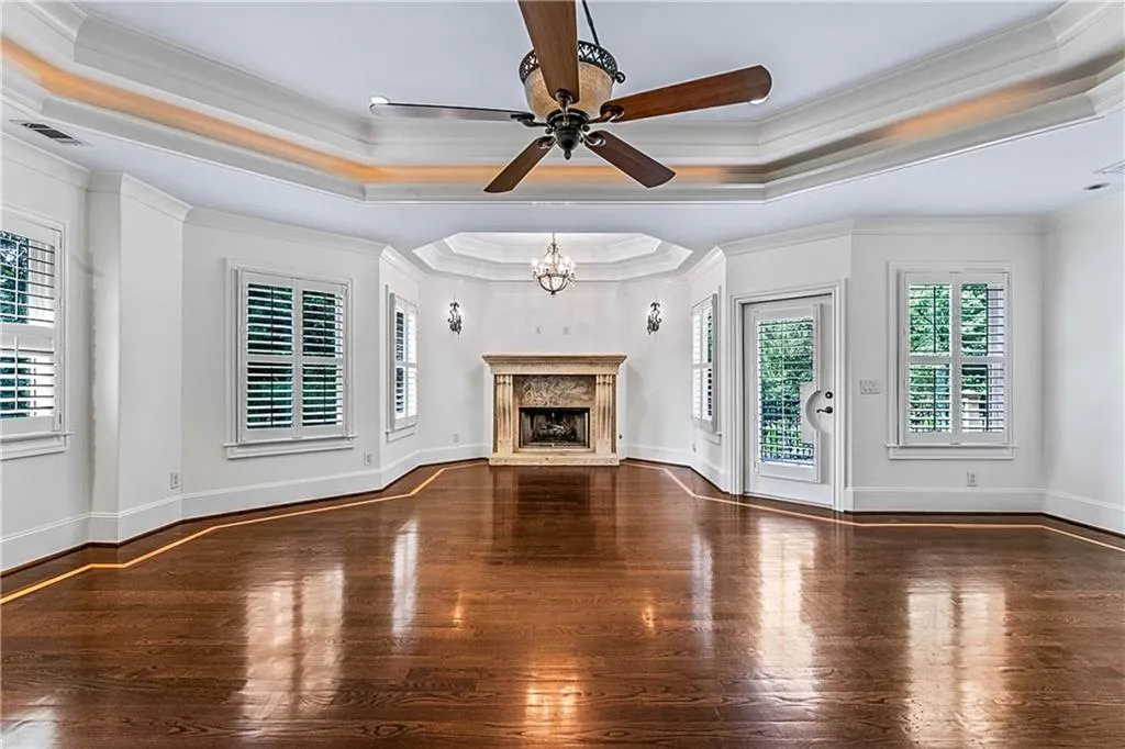 Unfurnished living room featuring a tray ceiling, dark wood-style flooring, crown molding, a chandelier, and a fireplace