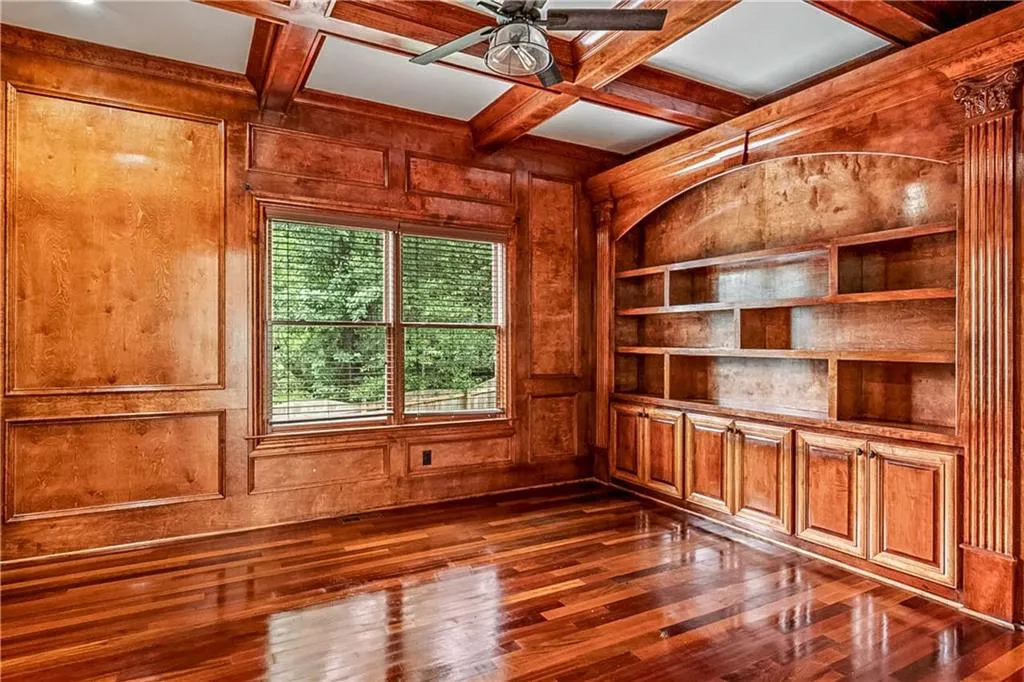 Elegant office with coffered ceiling, built in features, dark wood-style floors, wooden walls, and beam ceiling