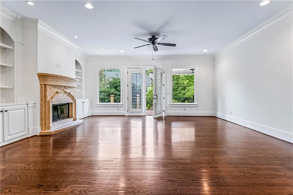 Unfurnished living room with crown molding, dark wood-type flooring, built in shelves, a high end fireplace, and a ceiling fan