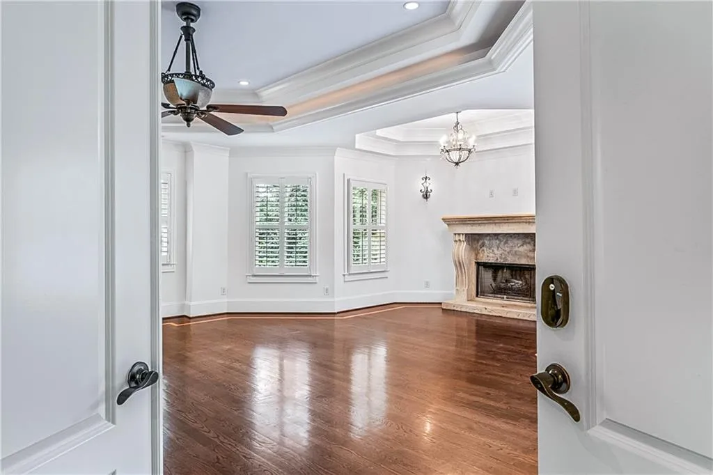 Unfurnished living room featuring a tray ceiling, dark wood finished floors, crown molding, a fireplace, and a chandelier