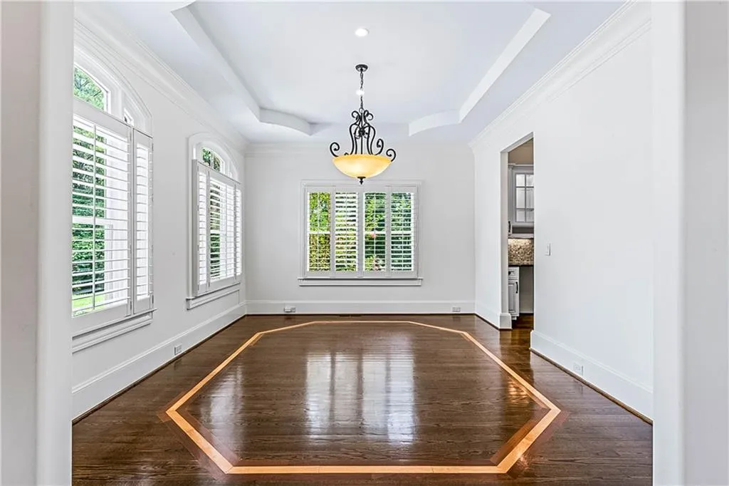 Unfurnished dining area with a raised ceiling, dark wood-style flooring, and crown molding