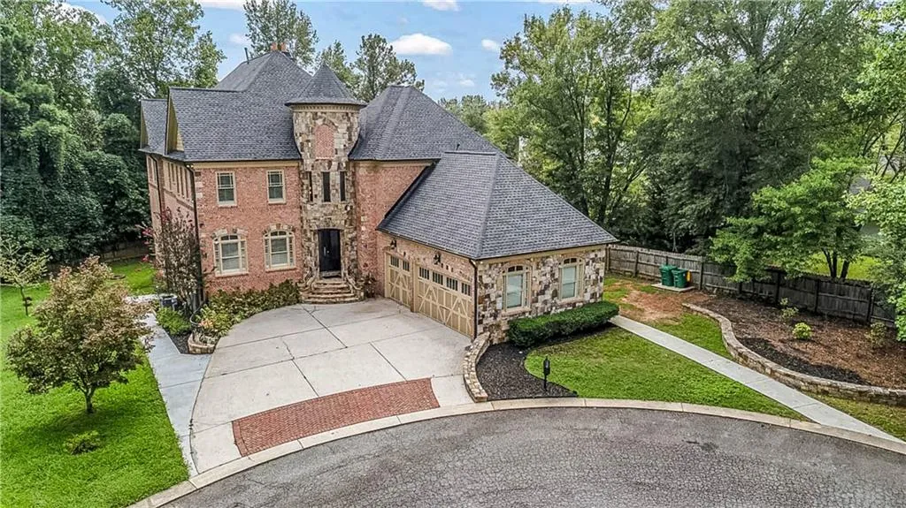 View of front of house featuring stone siding, an attached garage, driveway, a high end roof, and view of wooded area