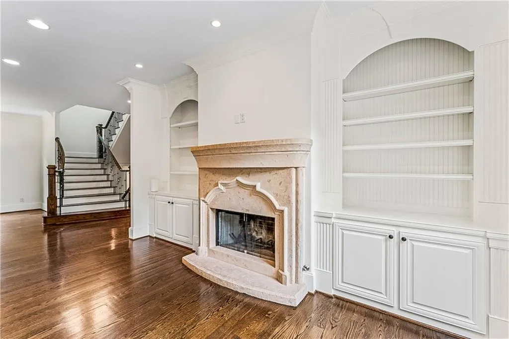 Unfurnished living room featuring built in shelves, a premium fireplace, stairway, dark wood-type flooring, and crown molding