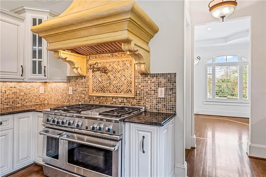 Kitchen with range with two ovens, white cabinetry, dark stone countertops, and custom range hood