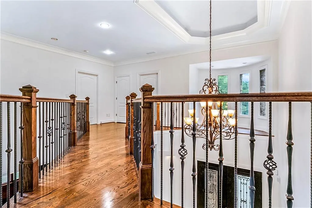 Hallway with crown molding, a chandelier, wood finished floors, and a raised ceiling
