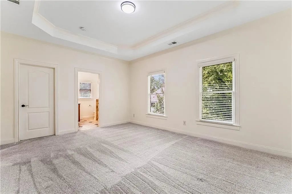 Unfurnished bedroom with a tray ceiling, light carpet, ensuite bath, and ornamental molding