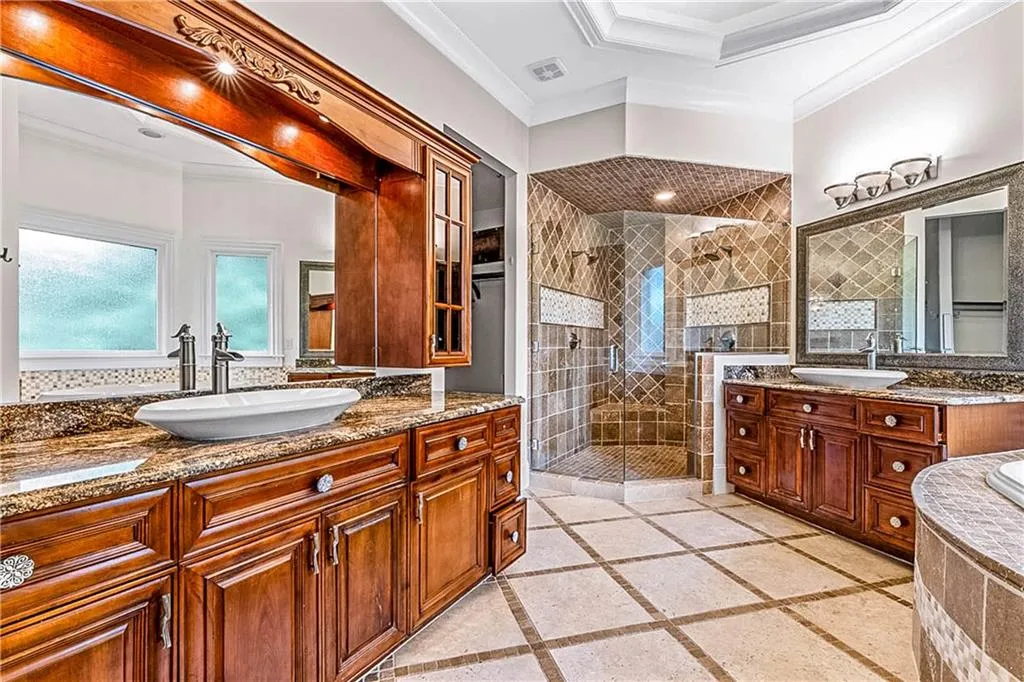 Full bathroom with a stall shower, crown molding, two vanities, and inlaid floor details