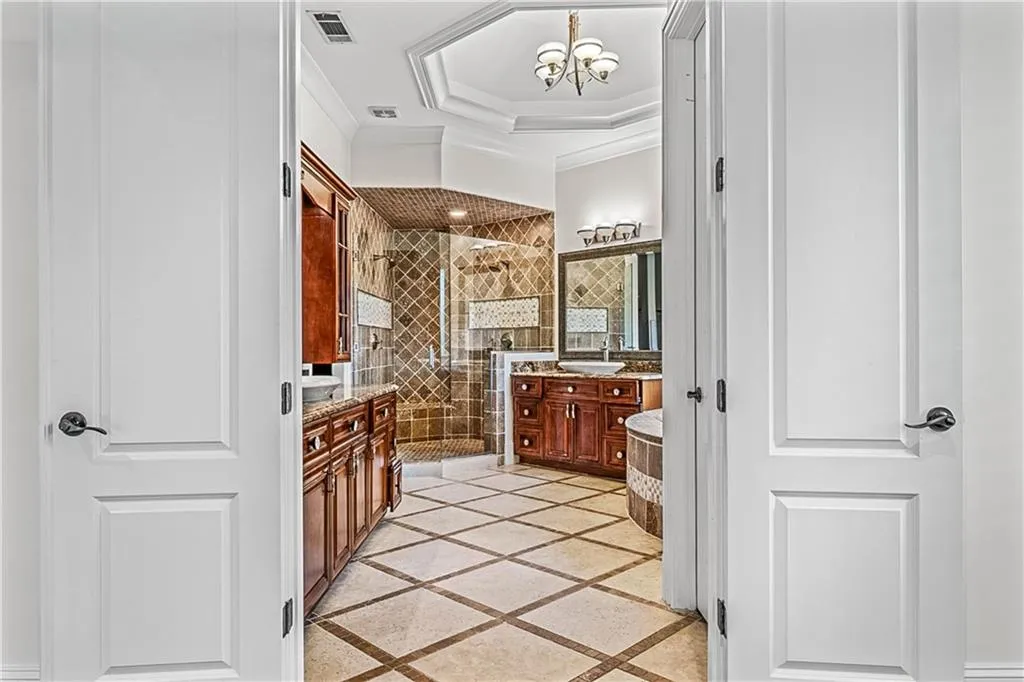 Bathroom featuring vanity, a shower stall, a tray ceiling, inlaid floor details, and ornamental molding