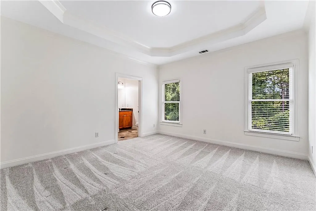 Unfurnished bedroom featuring a raised ceiling, multiple windows, light colored carpet, and crown molding