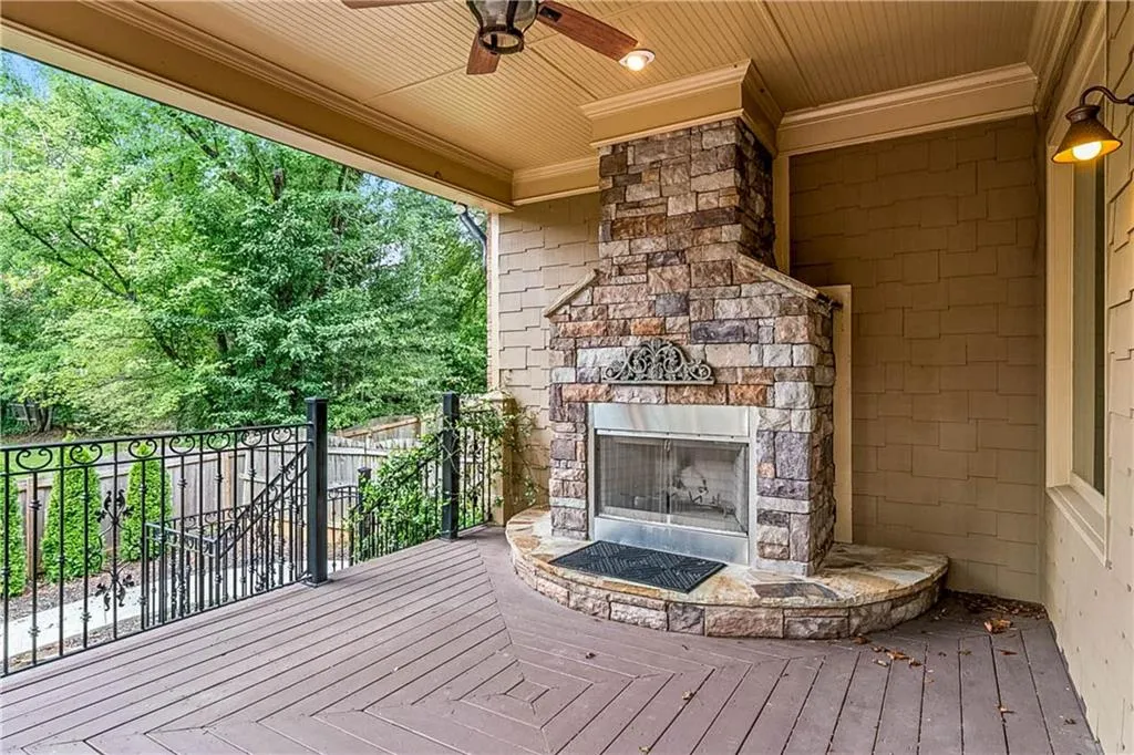 Wooden deck with an outdoor stone fireplace and a ceiling fan