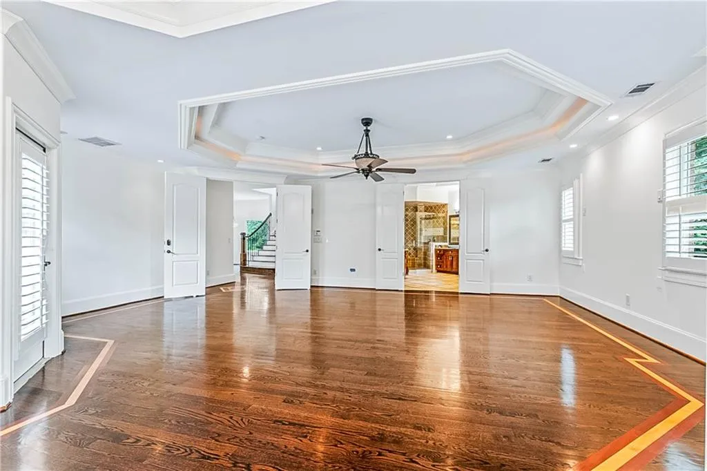 Luxury owners suite  with a raised ceiling, ornamental molding, wood-type flooring, ceiling fan, and stairway