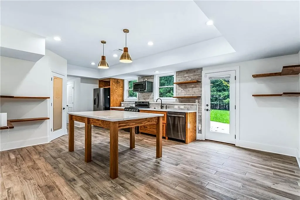 Kitchen with brown cabinetry, decorative light fixtures, recessed lighting, light wood-type flooring, and black appliances