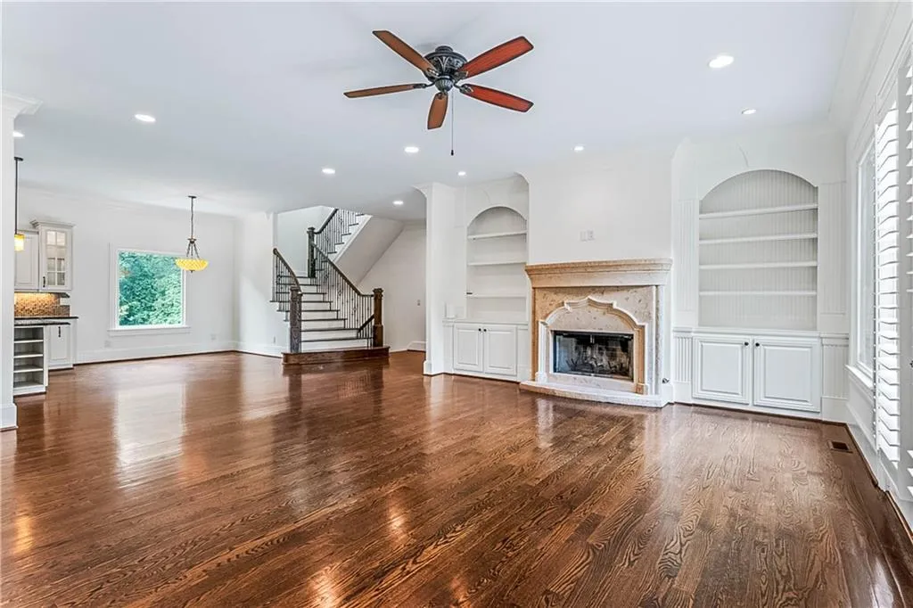 Unfurnished living room featuring a high end fireplace, dark wood-style flooring, a ceiling fan, stairway, and built in features