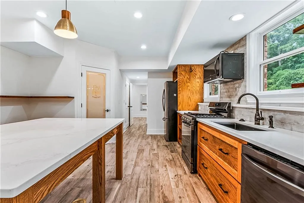 Kitchen featuring brown cabinets, light wood finished floors, recessed lighting, black appliances, and pendant lighting