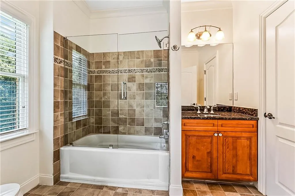 Full bathroom with bath / shower combo with glass door, vanity, crown molding, and light tile patterned flooring