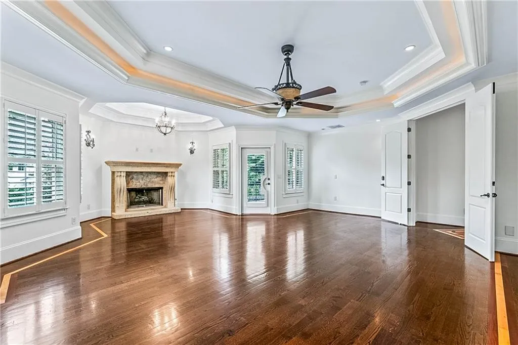 Unfurnished living room featuring a raised ceiling, dark wood-style flooring, ornamental molding, a fireplace, and recessed lighting
