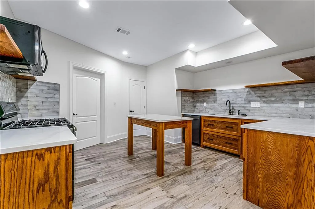 Kitchen featuring decorative backsplash, open shelves, light wood-style floors, light stone countertops, and range with gas cooktop