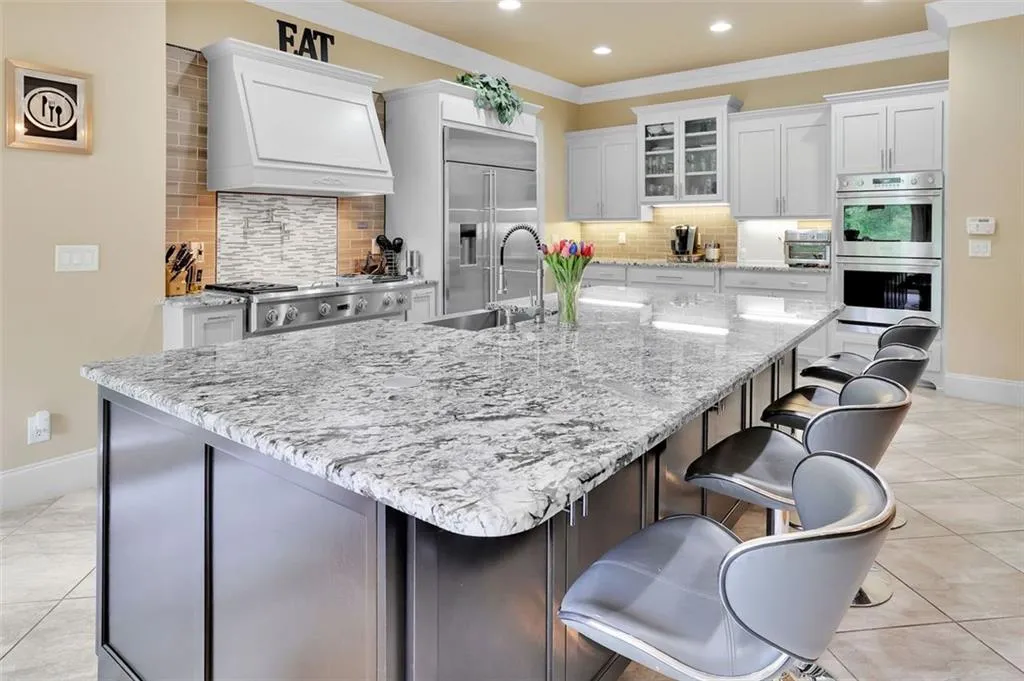 Kitchen with huge island featuring light tile floors, custom range hood, appliances with stainless steel finishes, and backsplash
