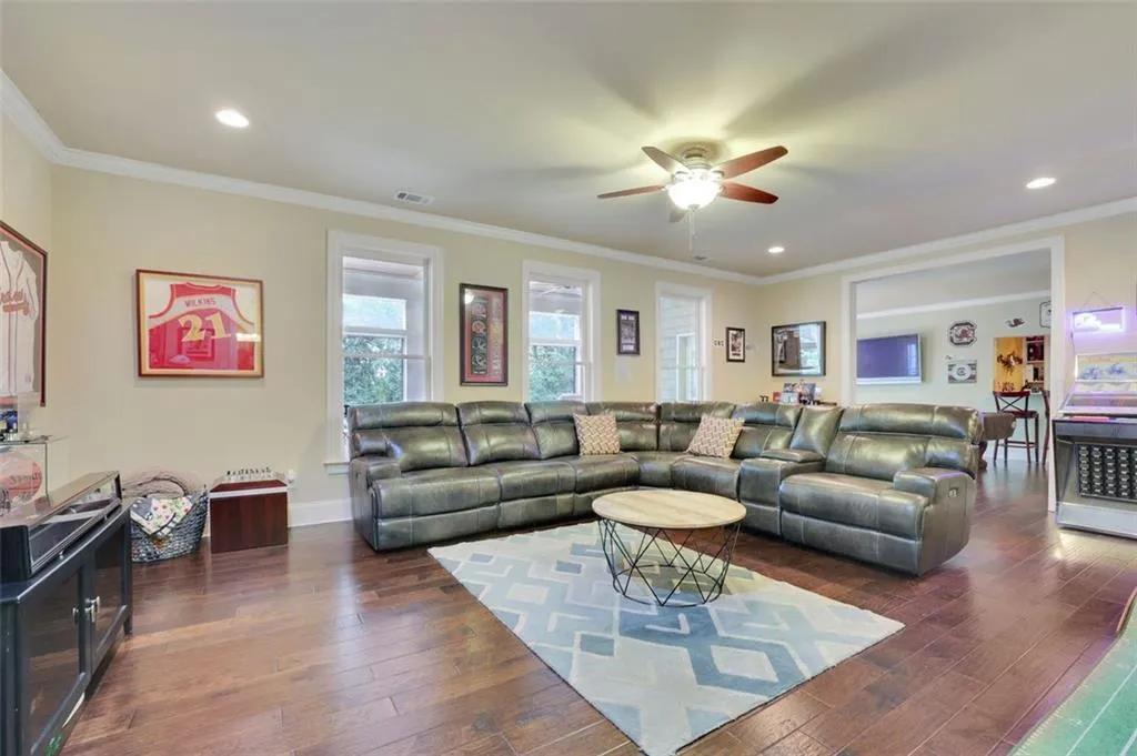Open lounge/sitting/family room featuring dark wood-type flooring, ceiling fan, and crown molding