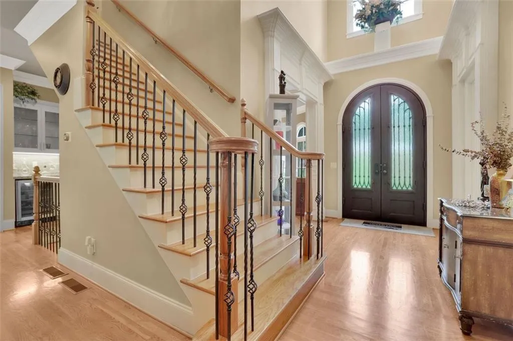 Foyer entrance with French iron doors, beverage cooler, ornamental molding, and light hardwood / wood-style floorsoverlooking screened porch and tree tops, ceiling fan, a fireplace, coffered ceiling, and light wood-type flooring