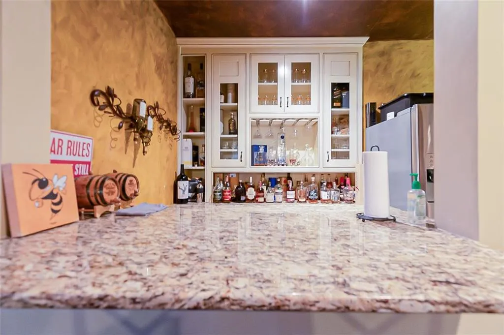 Custom built bar with refrigerator with ice dispenser, white cabinets, and light stone countertops and sink