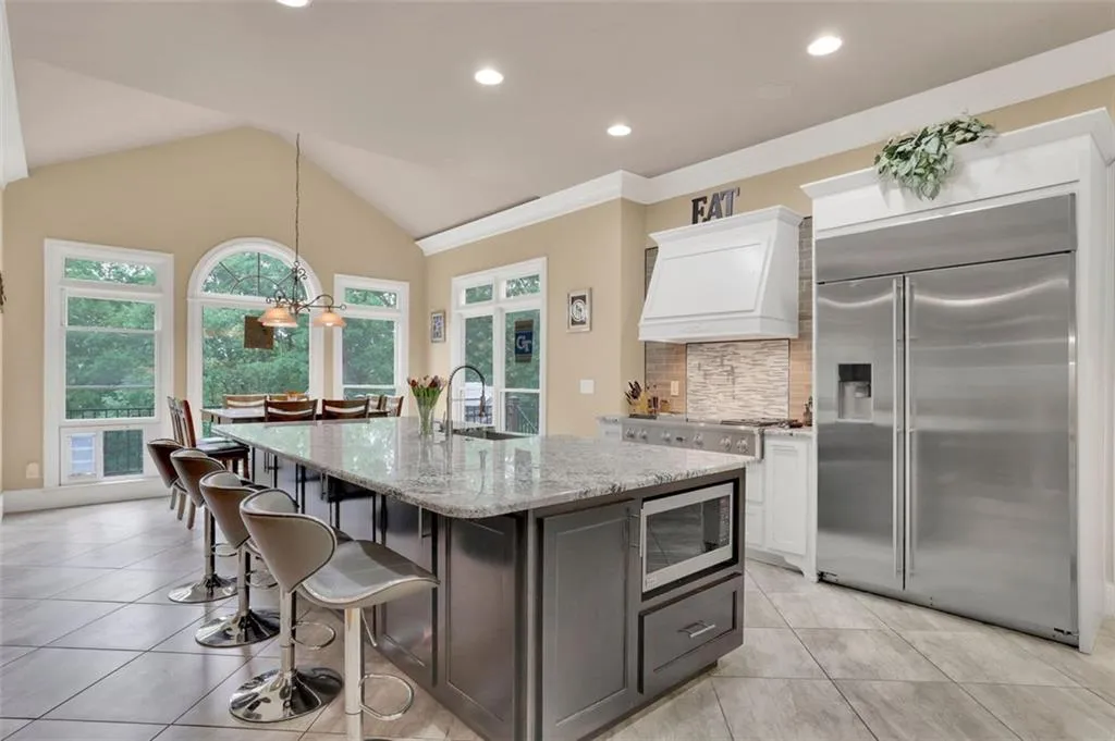 TKitchen featuring custom range hood, vaulted ceiling, built in appliances, a center island with sink, and white cabinetry