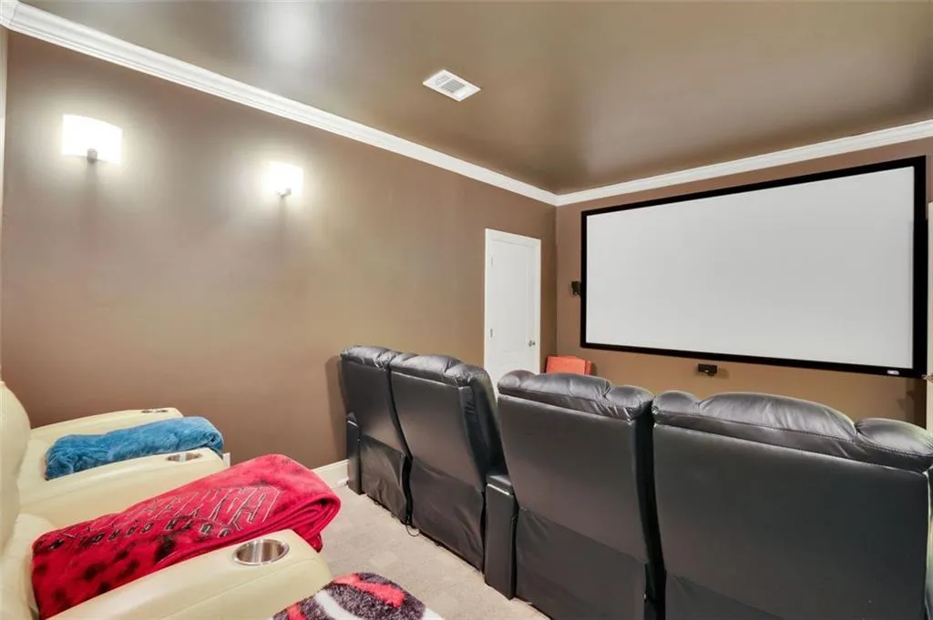 Cinema room with projector, screen and equipment closet featuring light colored carpet and ornamental molding