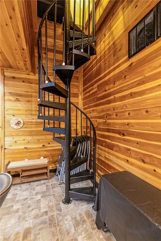 Spiral staircase from basement to sub basement featuring wooden walls and light tile floors. Can also access basement and sub basement from exterior stairs and daylight entry