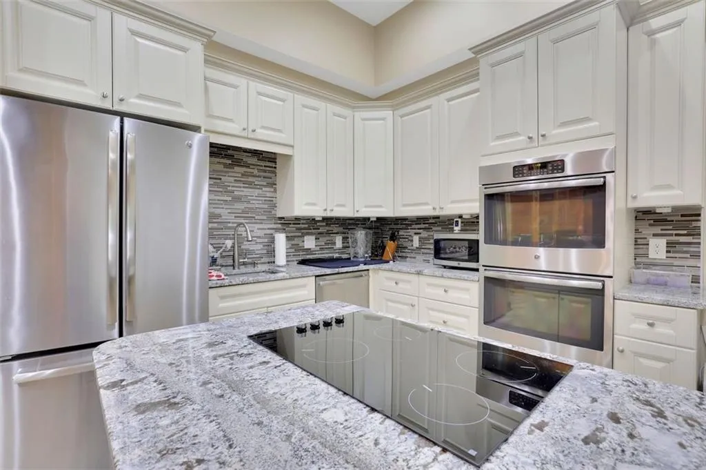 2nd full Kitchen (sub basement level)with sink, white cabinets, tasteful backsplash, and appliances with stainless steel finishes