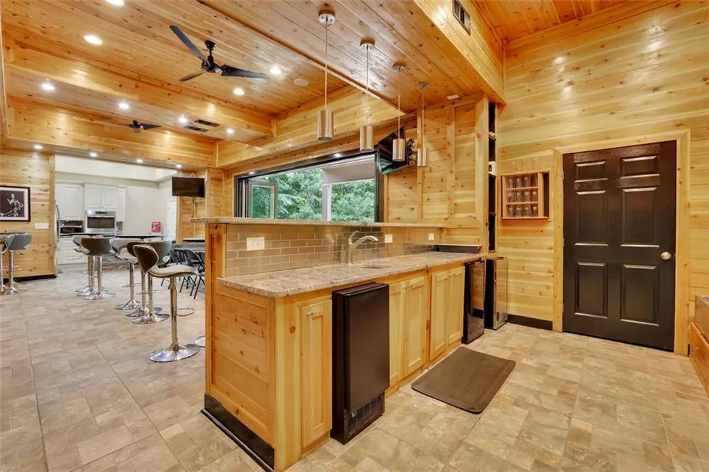 Bar (sub basement level) with light tile flooring, wooden ceiling, light brown cabinets, and ceiling fan