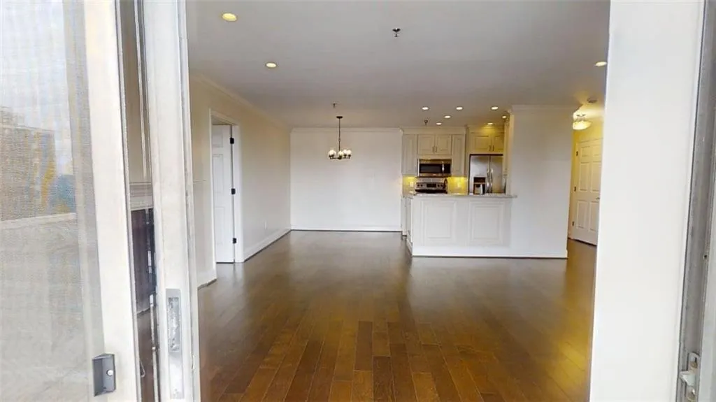 Unfurnished living room with a chandelier, crown molding, dark wood finished floors, and recessed lighting