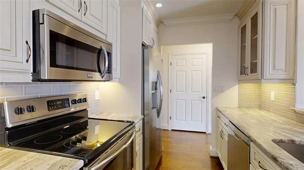 Kitchen featuring appliances with stainless steel finishes, tasteful backsplash, light stone countertops, glass insert cabinets, and dark wood-type flooring