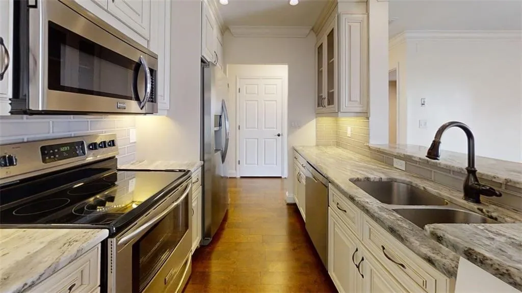 Kitchen featuring stainless steel appliances, light stone countertops, dark wood-type flooring, crown molding, and glass insert cabinets