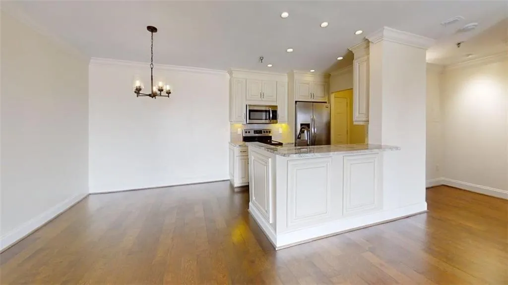 Kitchen featuring light stone counters, appliances with stainless steel finishes, crown molding, a chandelier, and decorative light fixtures