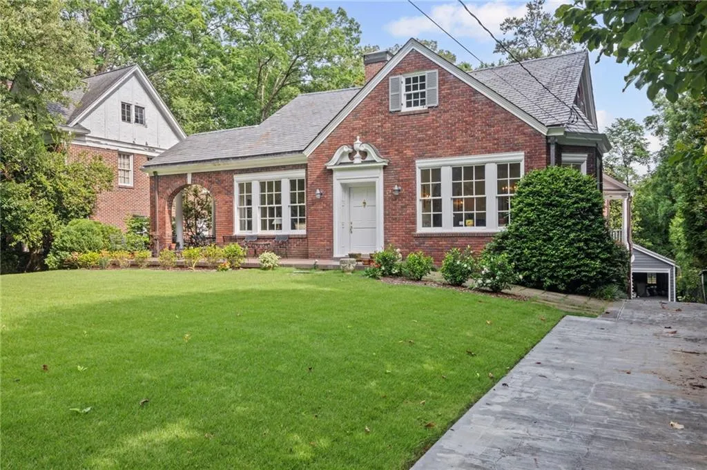 View of front of house with brick siding, a front yard, a chimney, slate roof and driveway to garage