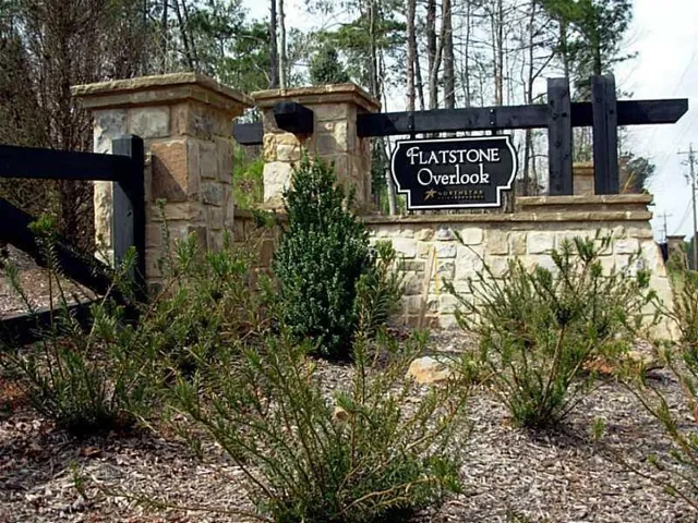 Stone and timber entrance monument featuring a custom sign, established plantings, and natural mulch beds