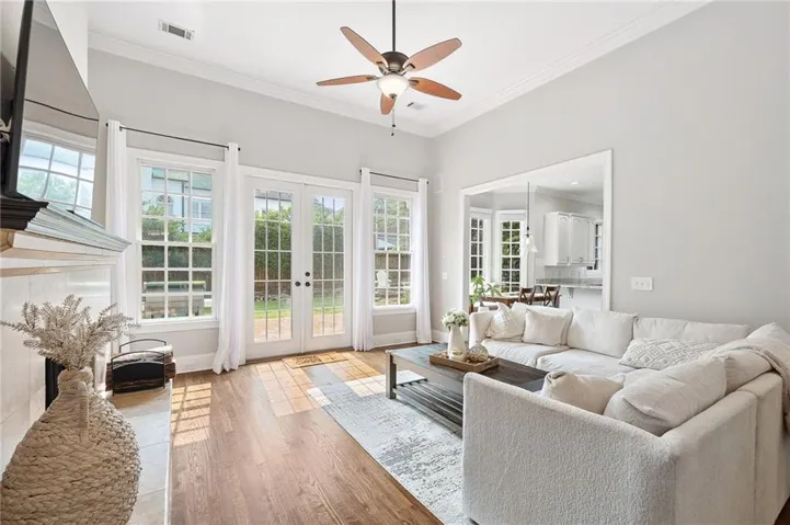 Spacious living area featuring wood-finish flooring, a fireplace with a stone surround and mantel, and high ceilings with crown molding
