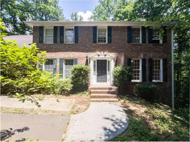 Brick exterior with white windows, dark shutters, and a decorative front door surround