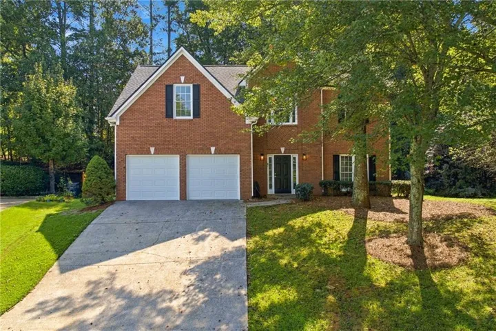 Brick exterior with a gabled roofline, two-car garage, concrete driveway, and mature landscaping