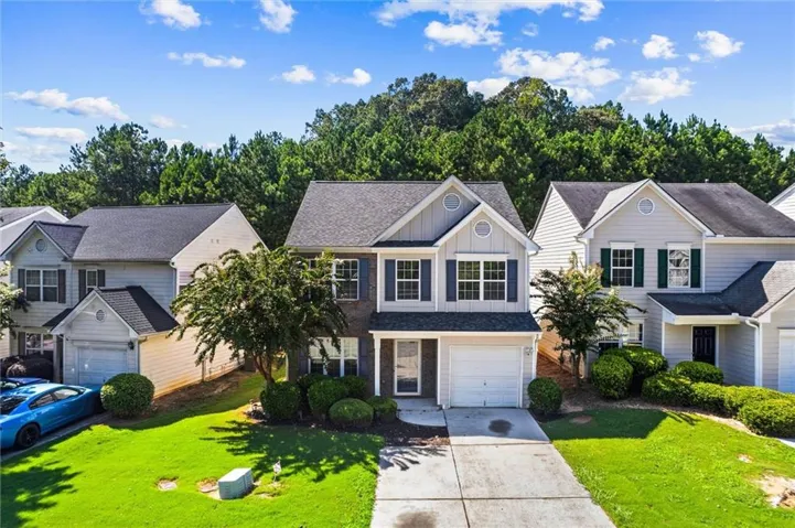 Two-story residence featuring a gray and white facade, an attached single-car garage, mature landscaping, and a paved driveway