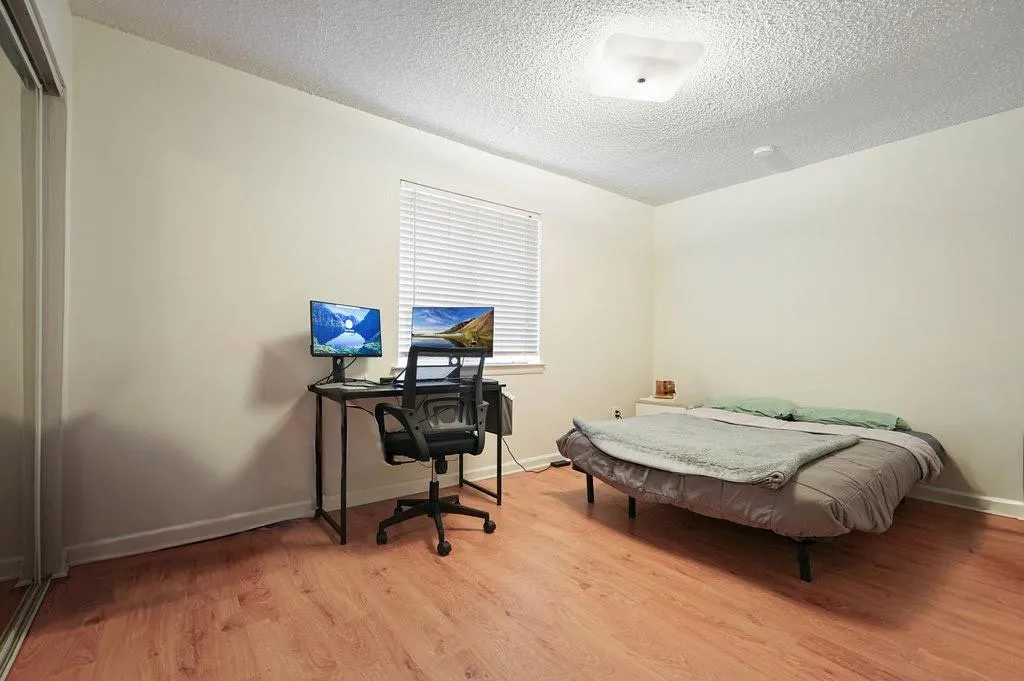 Bedroom with light wood-type flooring, an office area, and a textured ceiling