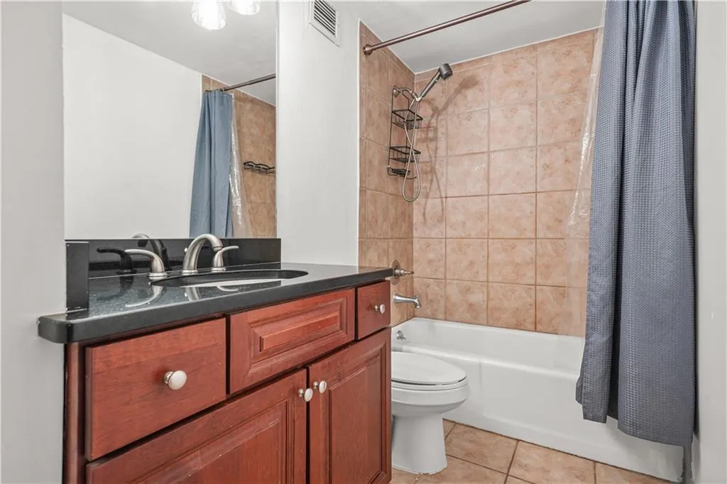 Bathroom featuring shower / tub combo with curtain, light tile patterned floors, and vanity