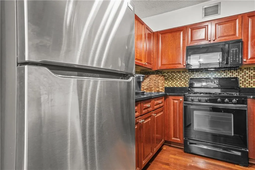 Kitchen with black appliances, tasteful backsplash, dark wood-style flooring, a textured ceiling, and brown cabinets