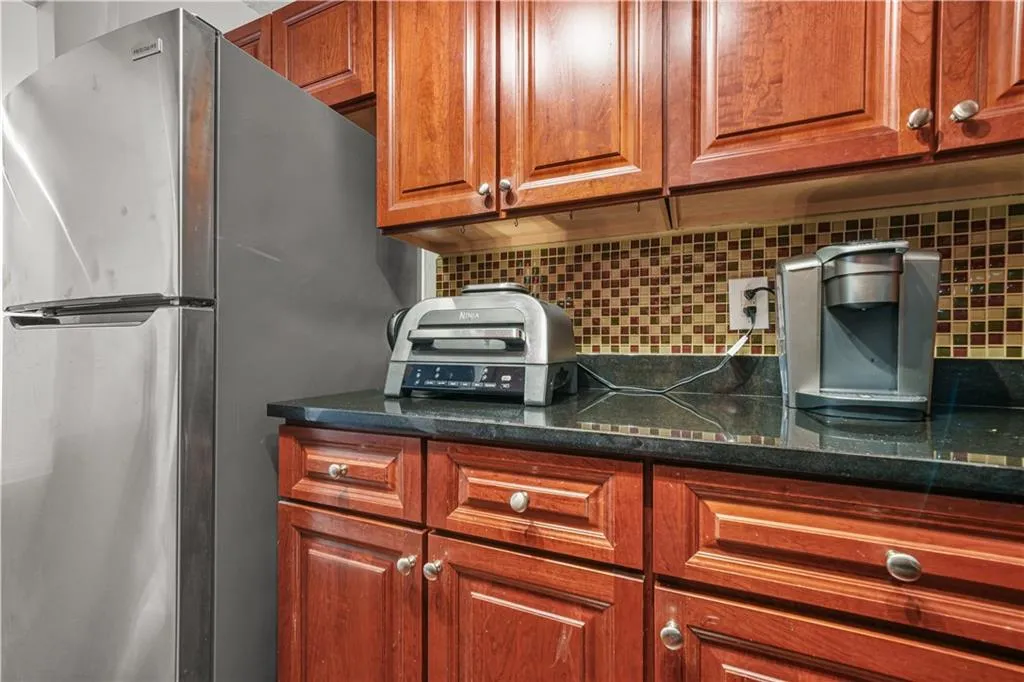 Kitchen with tasteful backsplash, brown cabinets, freestanding refrigerator, and dark stone counters