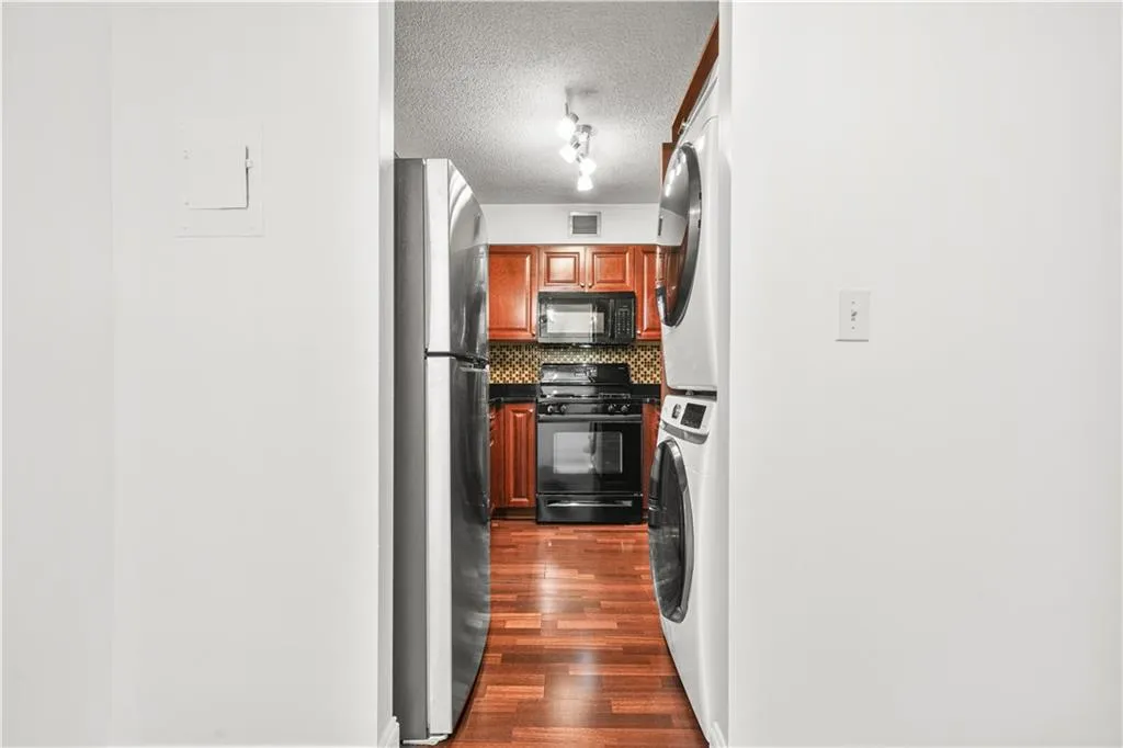 Kitchen featuring backsplash, black appliances, dark wood-type flooring, a textured ceiling, and stacked washer / dryer