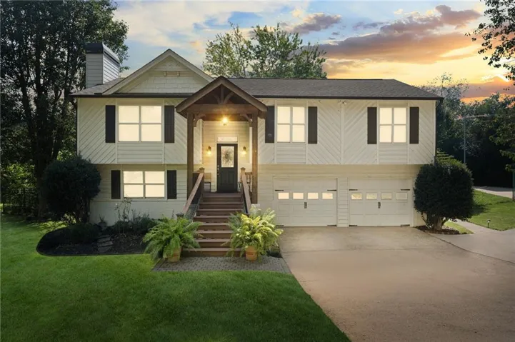 Split-level residence featuring a covered front entry, attached two-car garage, and a lush green lawn with mature landscaping