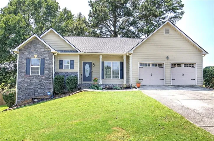 Welcoming ranch-style home featuring a stone and siding exterior, double two-car garage with paneled doors, and a manicured front lawn anchored by mature landscaping